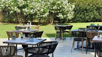 An outdoor patio area with tables and chairs, surrounded by a garden with flowering trees.