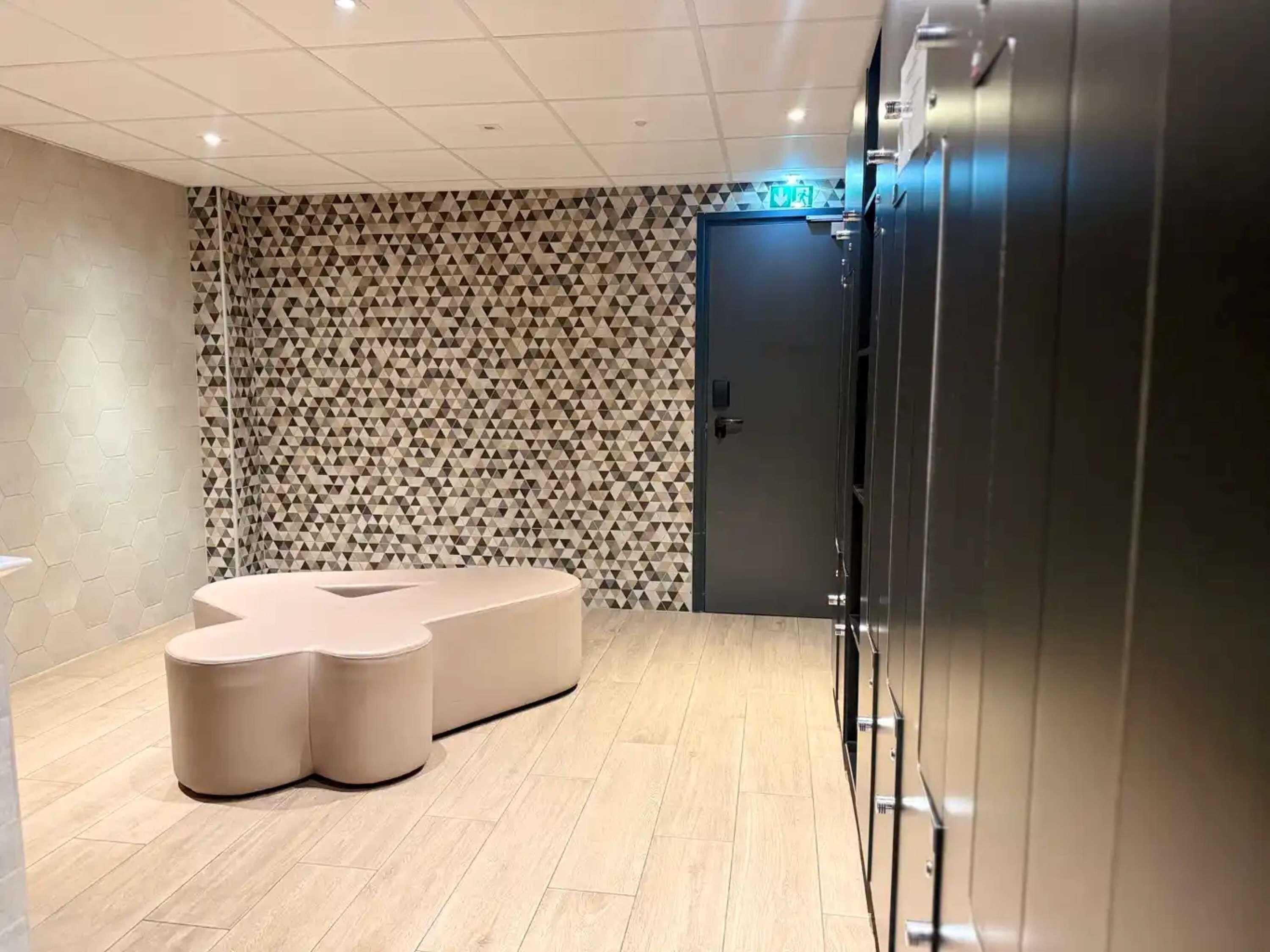 Ein modernes Zimmer mit einer Wand im geometrischen Muster, einer dunklen Tür und einer Sitzecke mit hellem Boden.