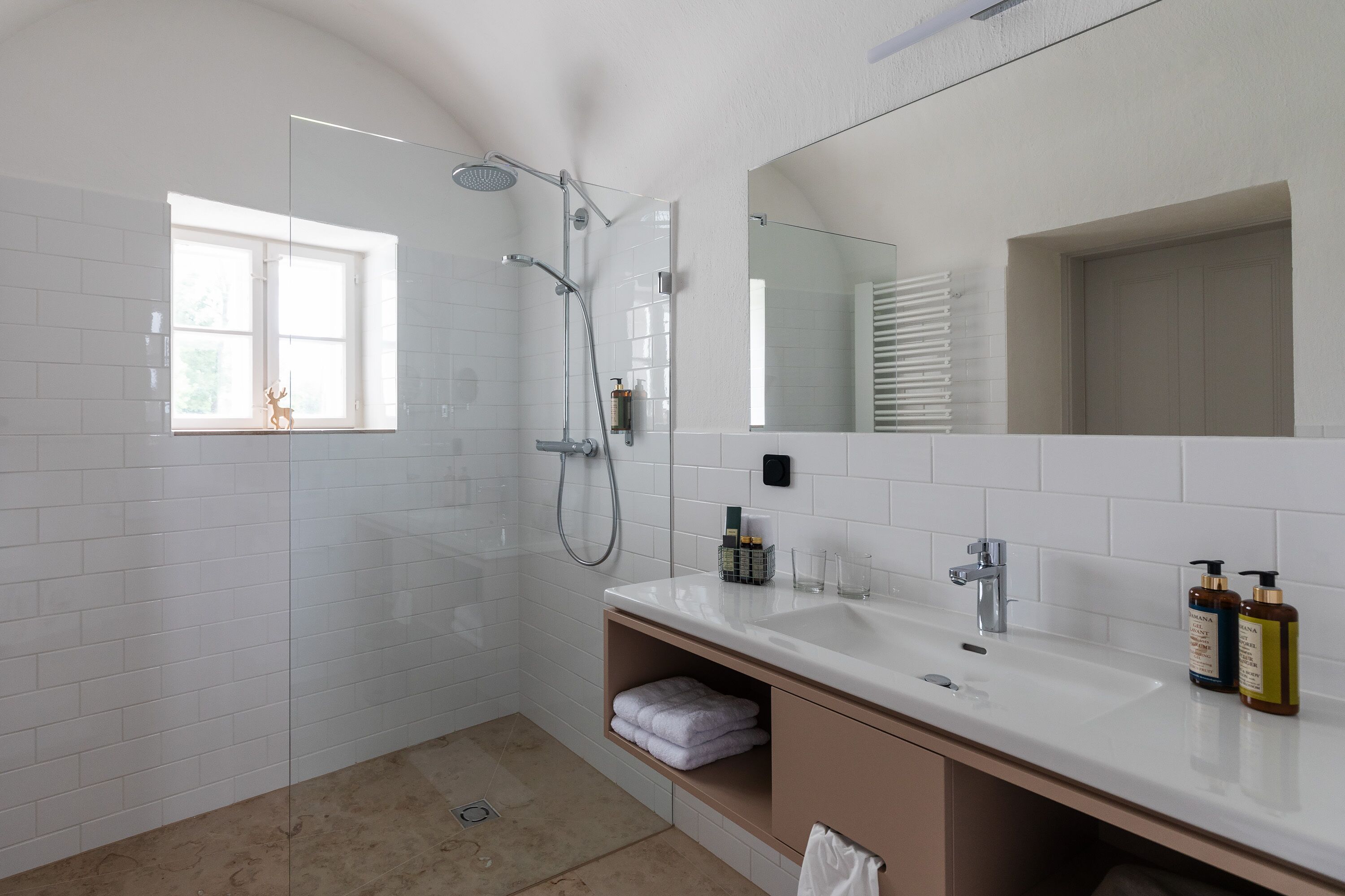 A modern bathroom with a glass-enclosed shower, a large mirror, and a vanity with a sink and storage.