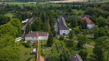 An aerial view of a rural village with traditional houses, green fields, and a central white building with a red roof.