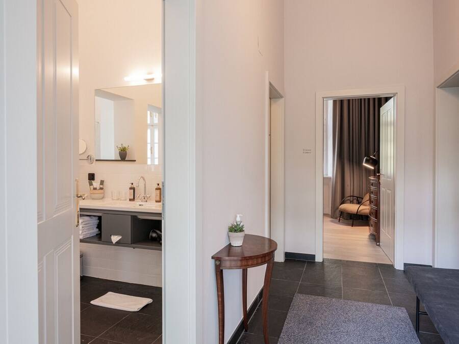 A modern hallway with a bathroom featuring a sink, mirror, and towel rack. A small table with a plant is placed in the hallway.