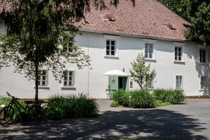 A white building with multiple windows and a door, surrounded by greenery and a bicycle. - Boutique Hotel Zum Oberjäger (Lackenbach)