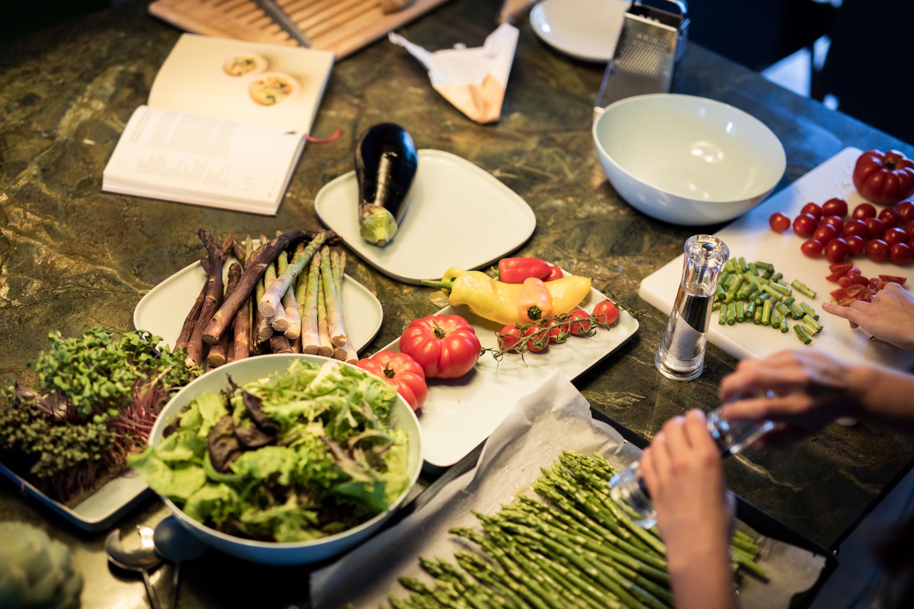 A kitchen counter with various vegetables, a cutting board, and a person preparing food.