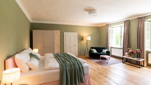 A bedroom with a bed, bedside table, lamp, and a window with curtains. - Boutique Hotel Zum Oberjäger (Lackenbach)