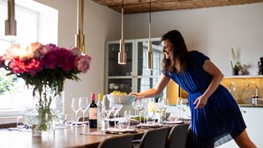 A woman in a blue dress serving food at a dining table with wine glasses and a vase of flowers. - Boutique Hotel Zum Oberjäger (Lackenbach)