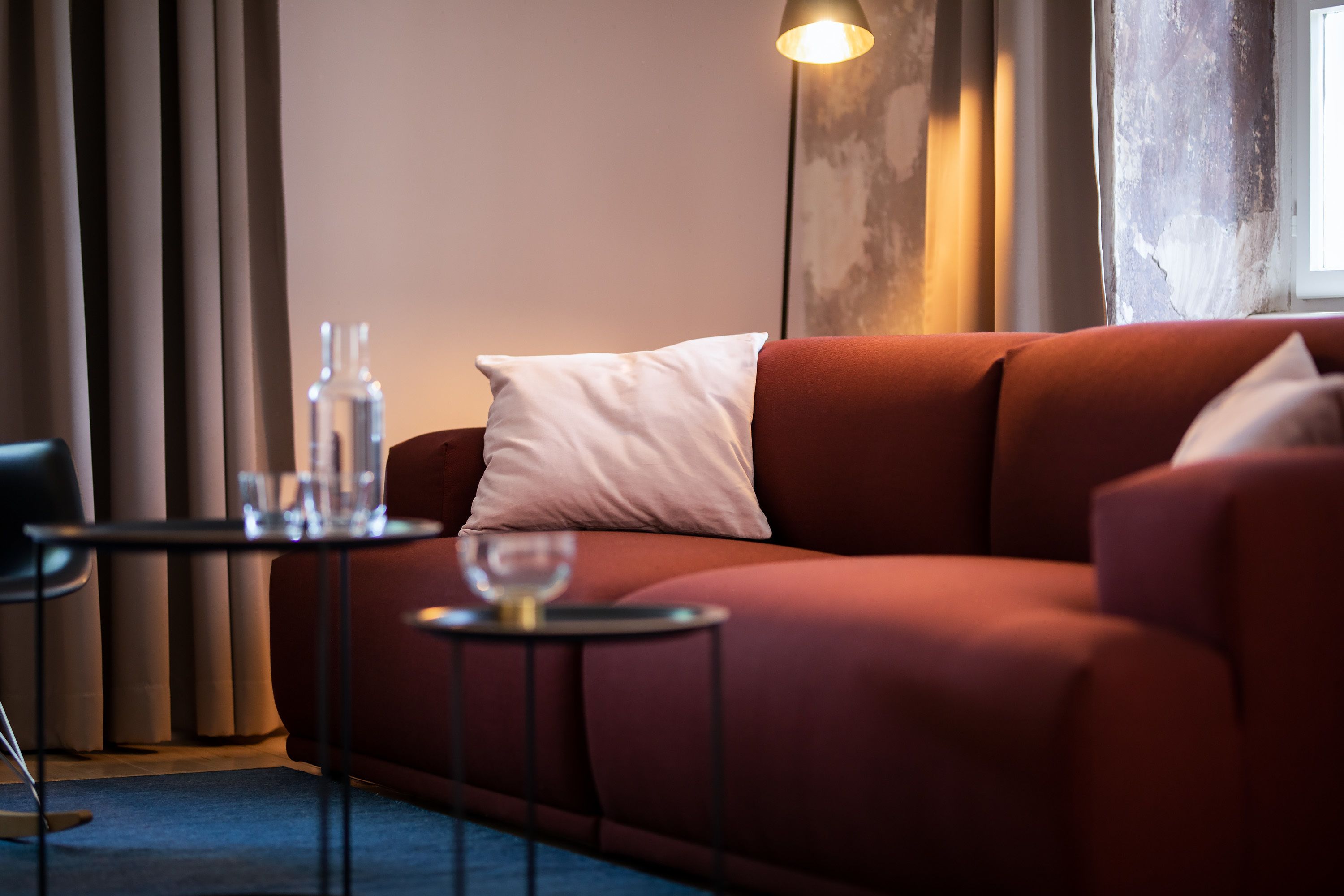 A modern living room with a red sofa, a small round table with a glass of wine, and a tall floor lamp.
