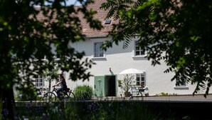 A white building with a green door, a bicycle parked in front, and a table with chairs outside. - Boutique Hotel Zum Oberjäger (Lackenbach)