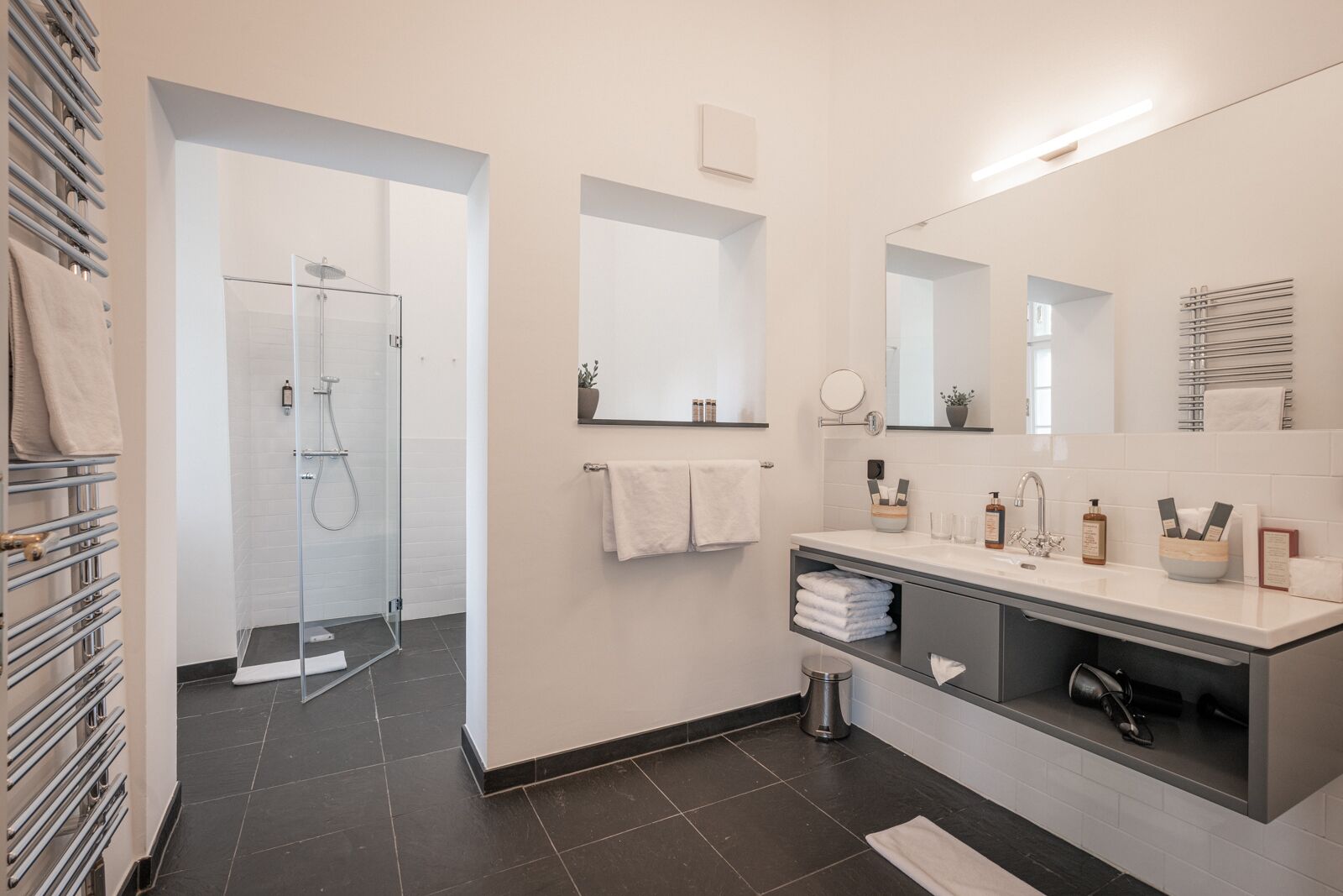 Ein modernes Badezimmer mit Glasdusche, Waschtisch inklusive Spiegel und einem Handtuchhalter.