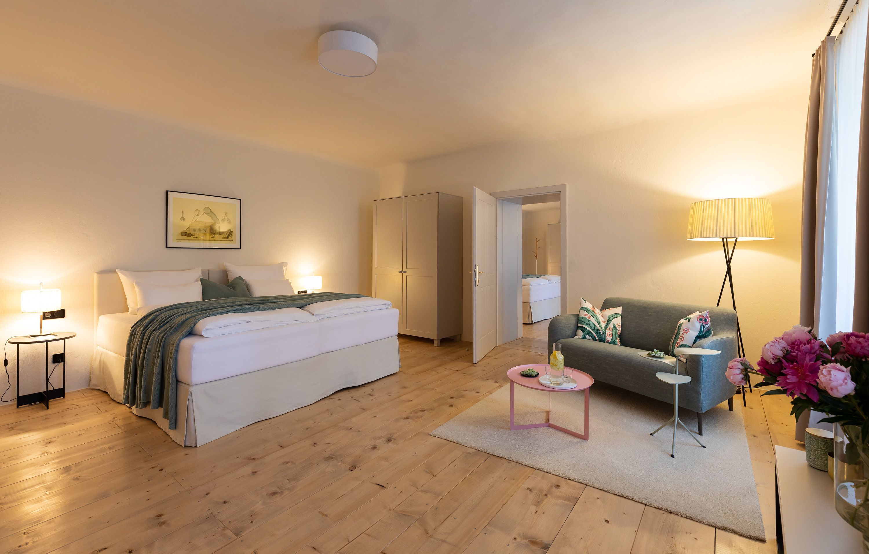 A modern bedroom with a large bed, bedside tables, a sofa, and a lamp.