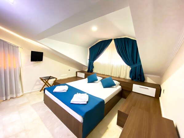 A modern hotel room with a large bed, a wooden nightstand, a flat-screen TV, and a window with curtains. - Zehra Hotel (Fethiye)