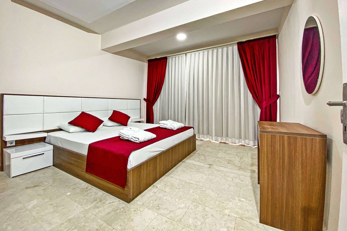 Une chambre d’hôtel avec un grand lit, une table de chevet en bois, une petite table de nuit et une armoire intégrée en bois.