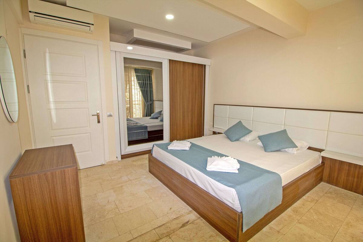 Une chambre à coucher comprenant un lit, une table de chevet en bois, une armoire et un miroir.