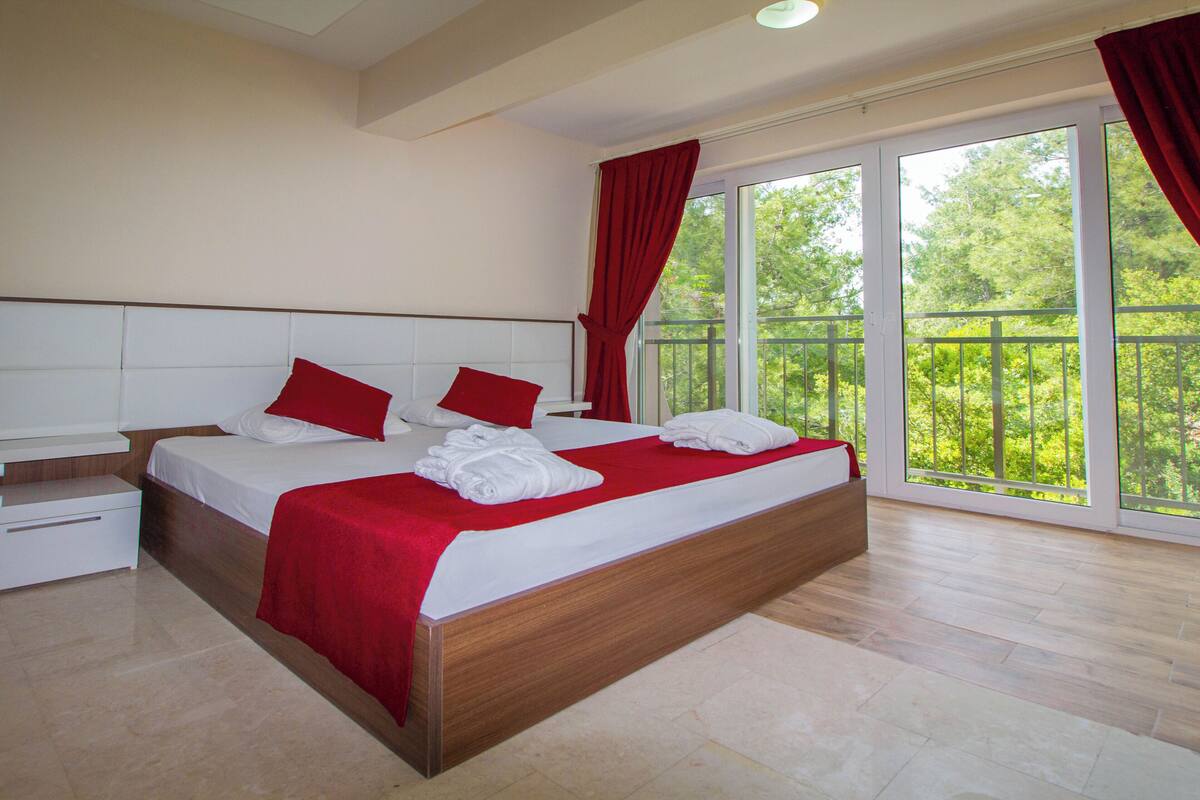 Une chambre avec un grand lit, une table de chevet et une fenêtre donnant sur un paysage verdoyant.