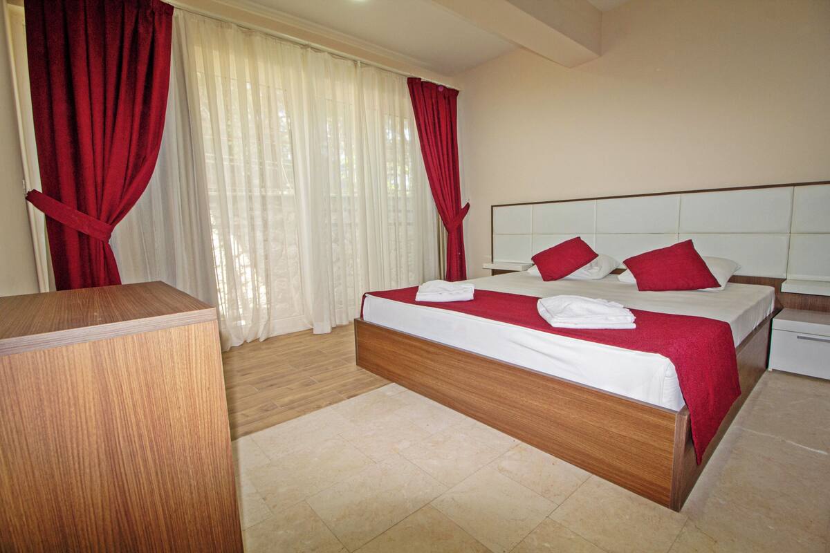 Une chambre d’hôtel avec un lit en bois, du linge de lit blanc, des rideaux rouges et une table de chevet.