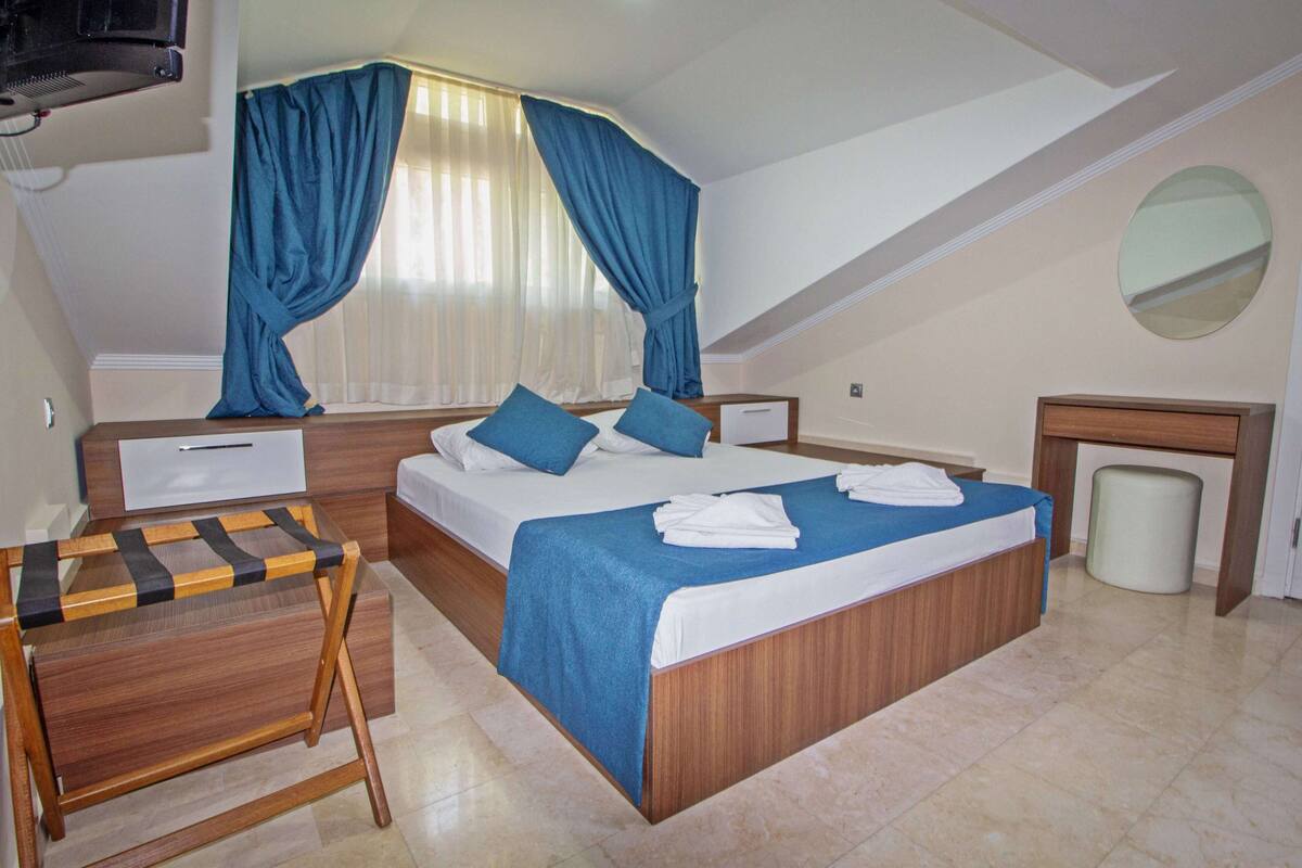 Une chambre à coucher avec un grand lit, un bureau en bois, une petite table, un miroir et une poubelle.