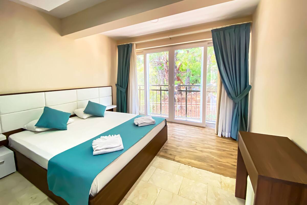 Une chambre d’hôtel avec un grand lit, une table de chevet en bois et une vue sur l’extérieur grâce à une porte-fenêtre coulissante.