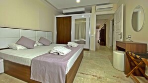 Habitación de hotel con una cama grande, cabecera de madera, mesita de noche, espejo y baño visible a través de una puerta abierta.
