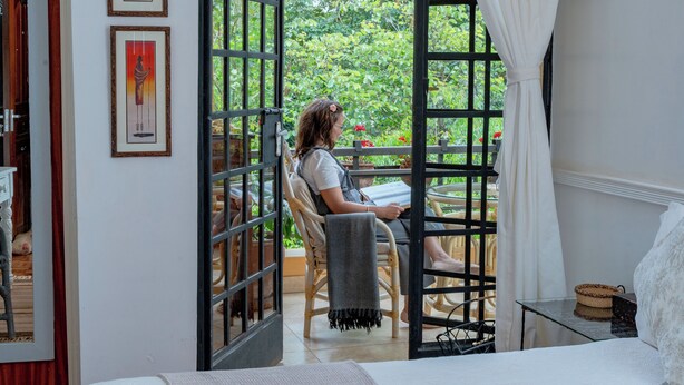 A room with a bed, a chair, a table, and a view of greenery outside. - Hob House (Nairobi)