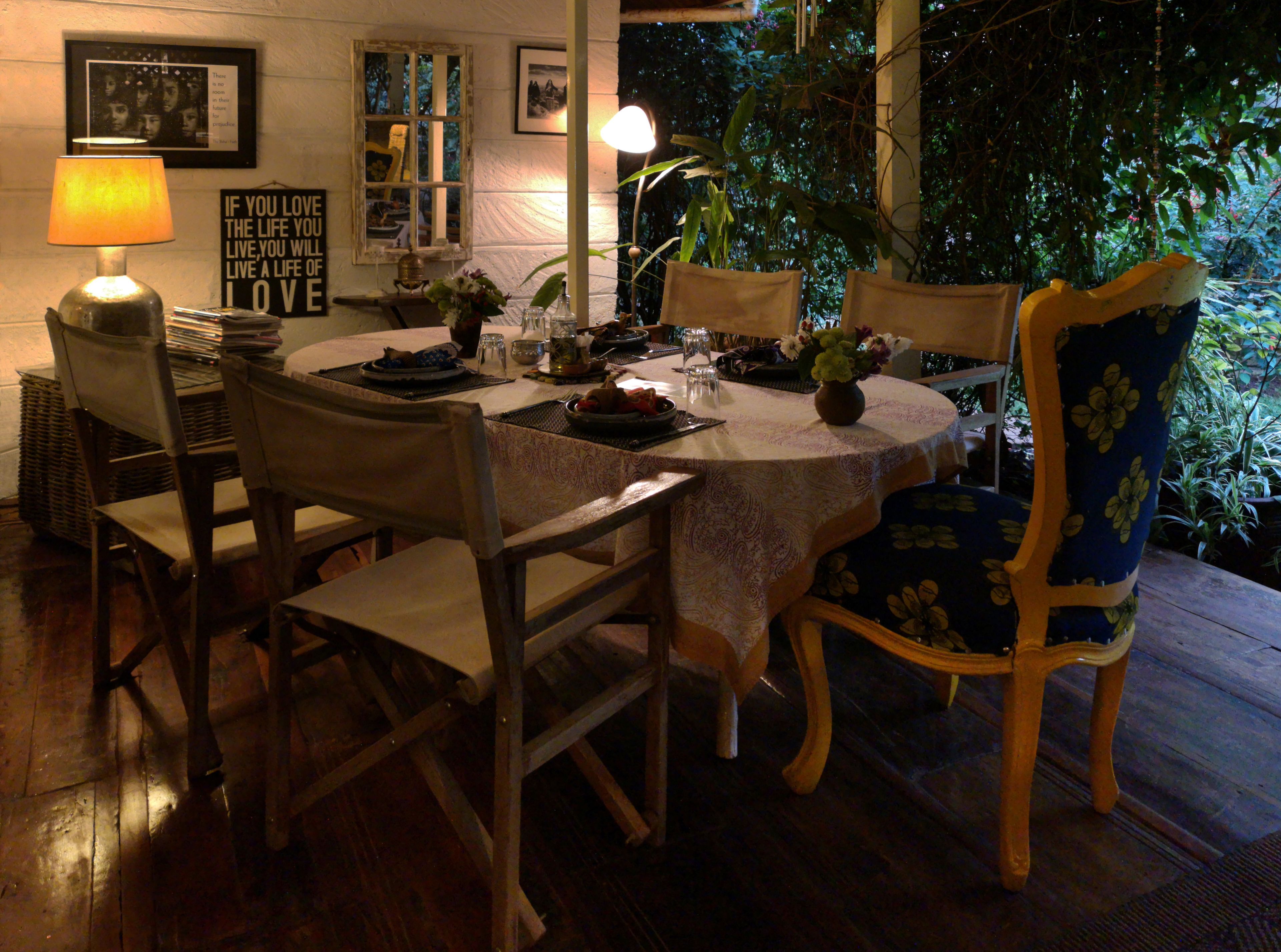 Mesa de comedor lista para cuatro personas, con sillas, una lámpara y una cita enmarcada en la pared.