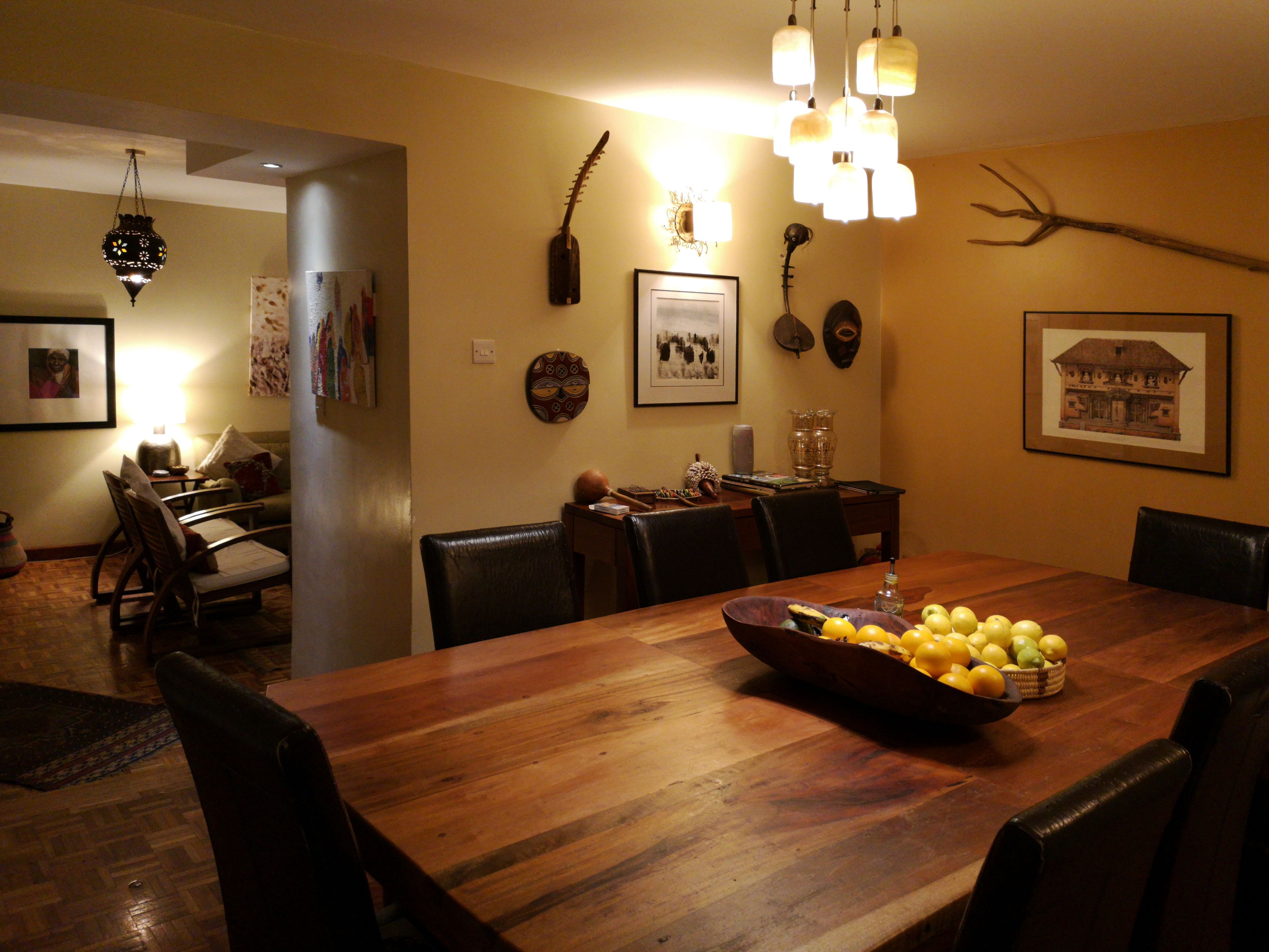 A dining area with a wooden table, chairs, and a bowl of lemons. There are wall decorations and a chandelier.