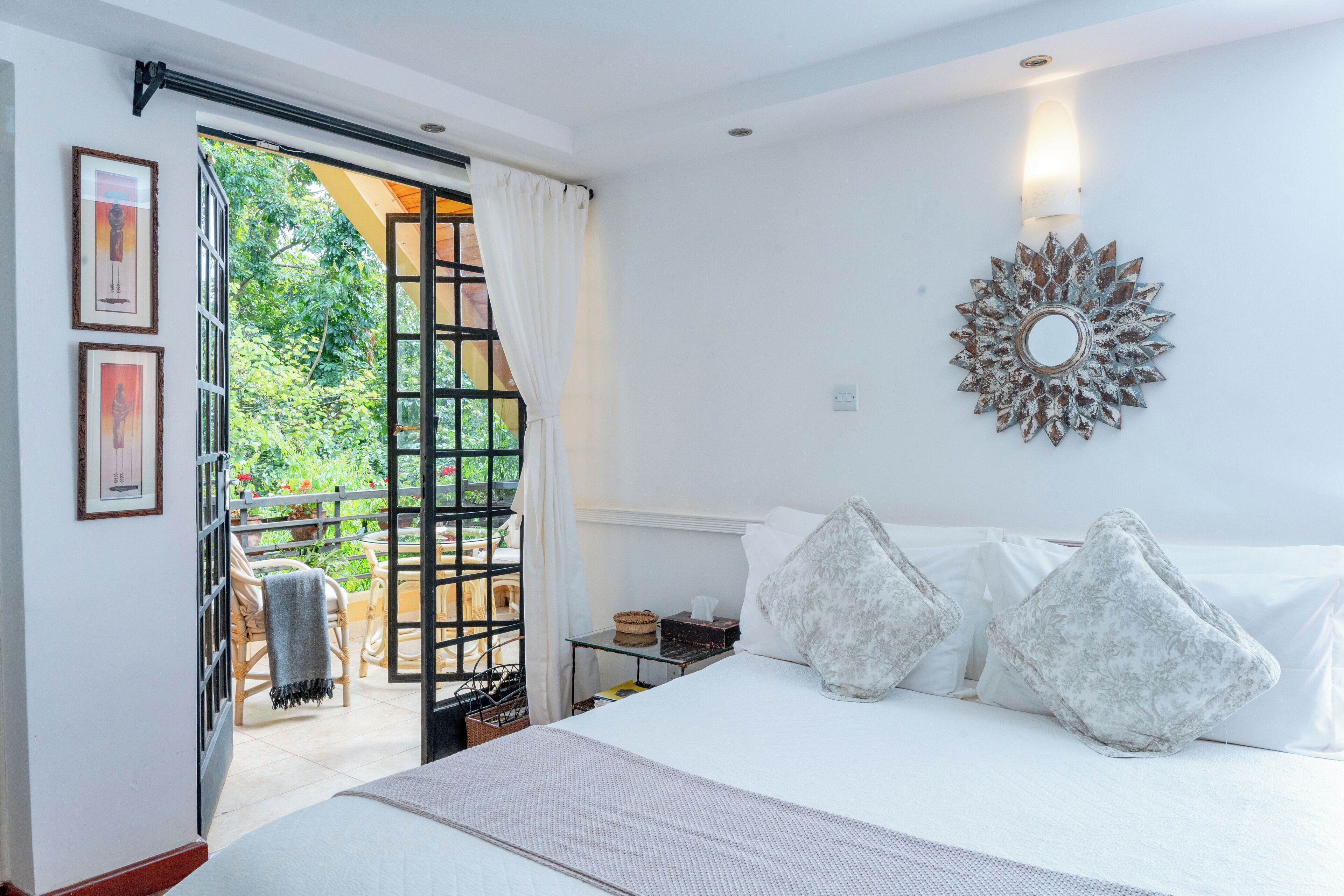 A bedroom with a large bed, a view through an open door to a balcony, and a decorative wall piece.