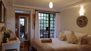 A bedroom with a bed, a desk, a mirror, and a window with a view of greenery. - Hob House (Nairobi)