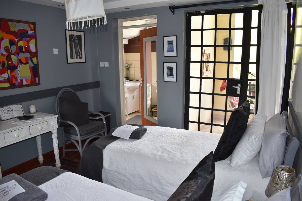 A hotel room with a bed, a desk, and a chair. There is a bathroom visible through an open door.