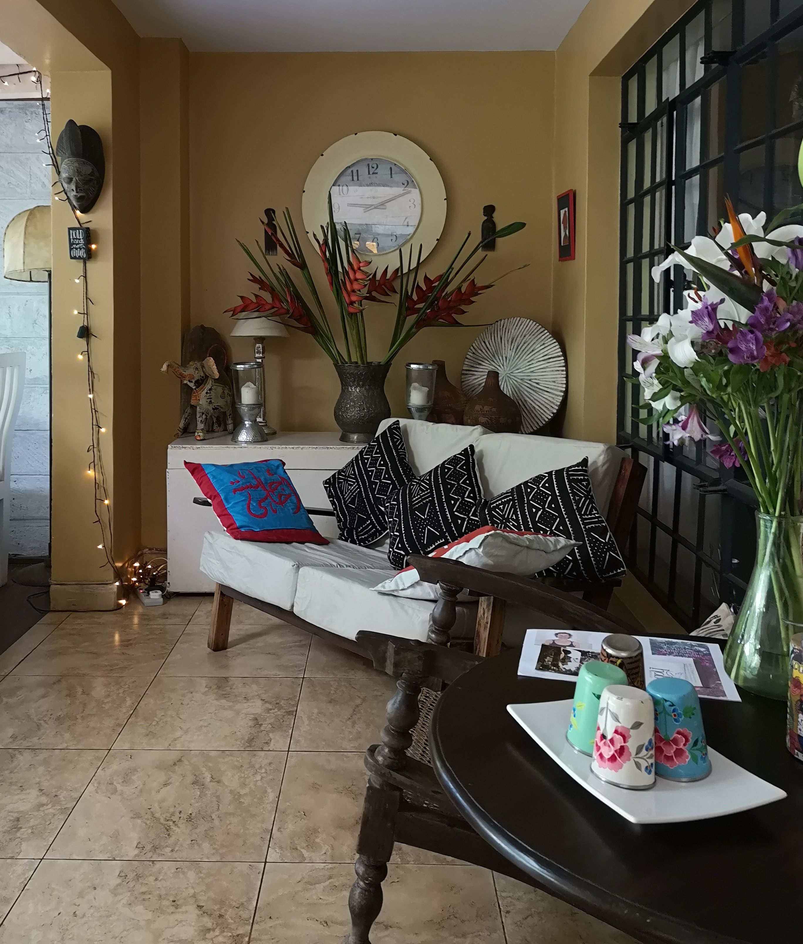 Una sala de estar con sofá, cojines decorativos, una mesa redonda con un florero y un reloj de pared.