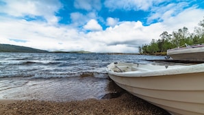 Een boot afgemeerd aan een kiezelstrand, met een bebost heuvel op de achtergrond.