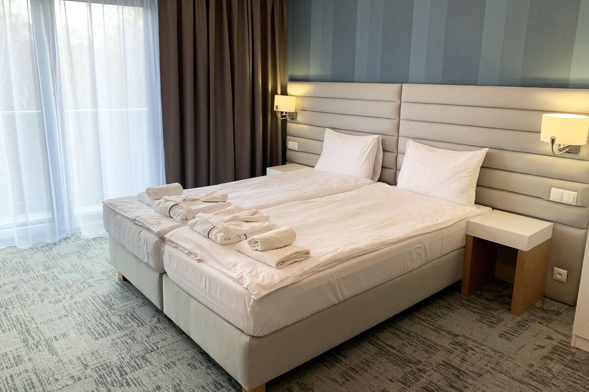 A modern hotel room with a large bed, a bedside table, and a headboard with integrated lighting.