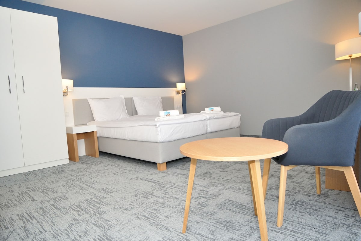 A hotel room with a bed, a chair, a table, and a wardrobe.