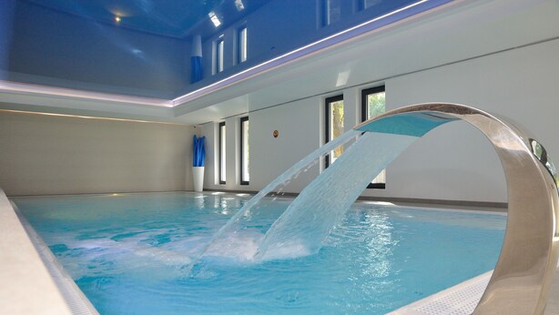 An indoor swimming pool with a water feature, clear blue water, and a modern design. - Hotel Hel (Hel)