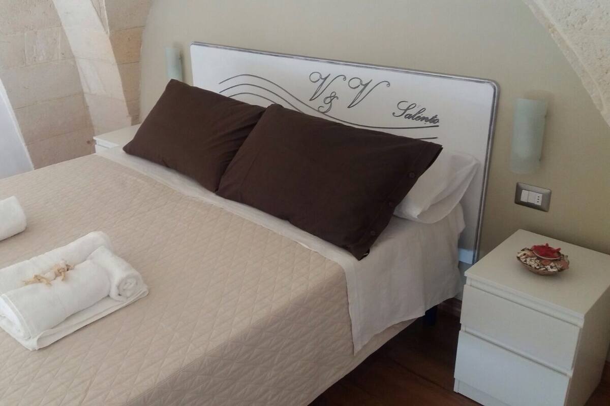Una cama hecha con dos almohadas marrones y dos toallas blancas enrolladas.