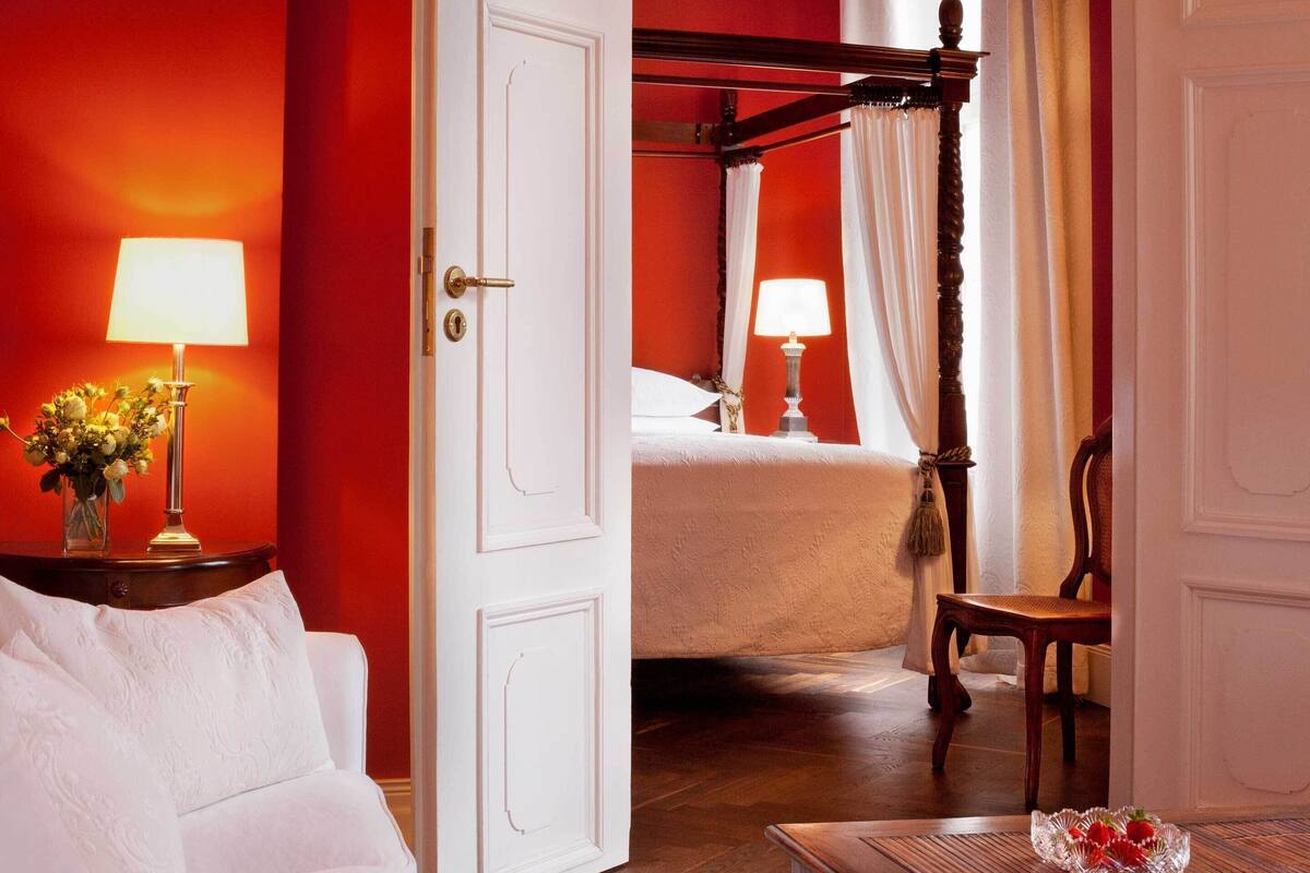 A hotel room with a bed, a sitting area with a chair, a nightstand with a lamp, and a vase with flowers.