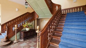 Una escalera de madera con peldaños azules, barandilla decorativa y un jarrón con flores sobre un aparador.