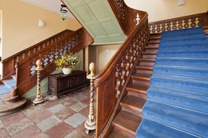 Una escalera de madera con peldaños azules, barandilla decorativa y un jarrón con flores sobre un aparador.