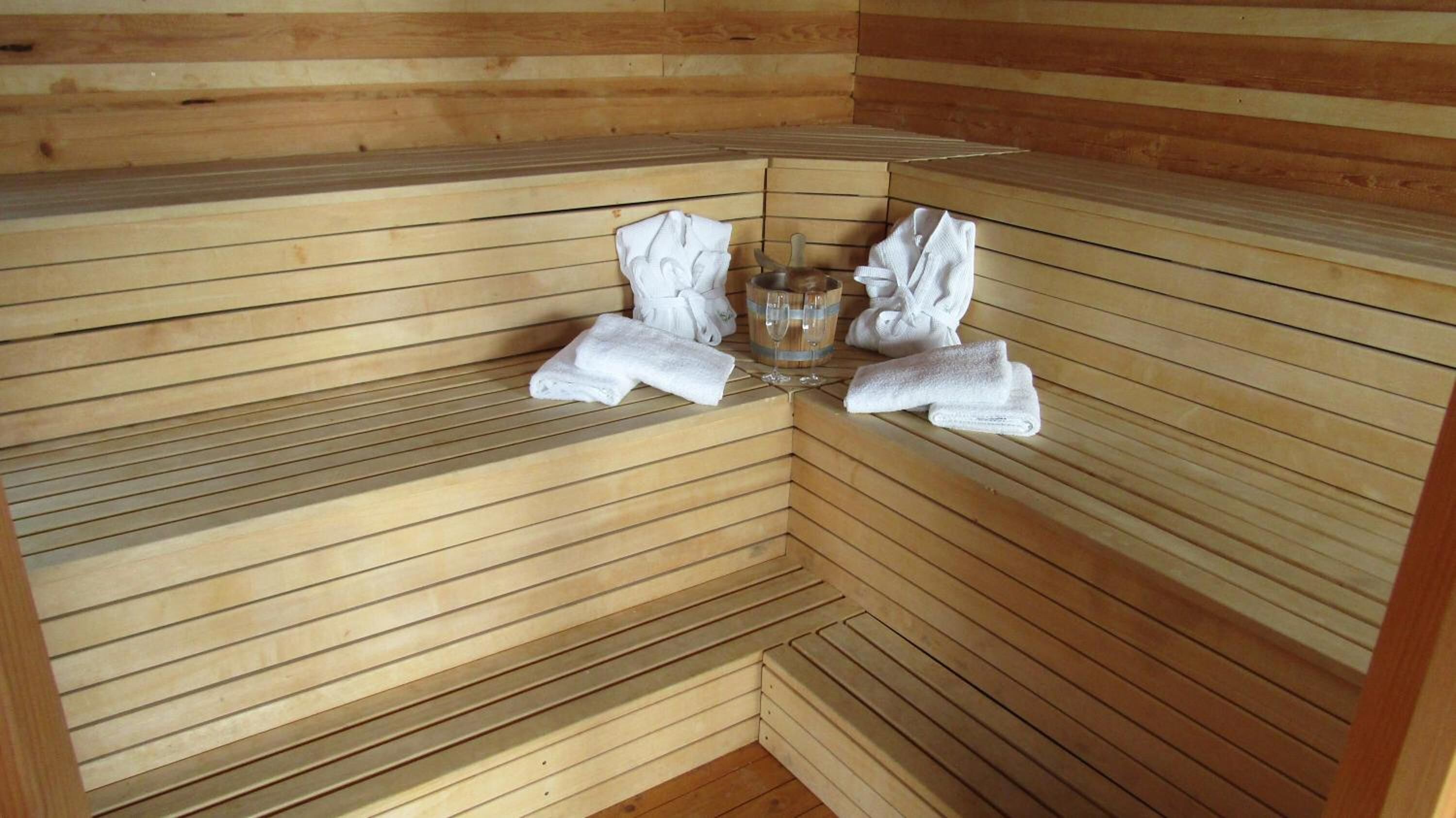 A sauna with wooden benches, towels, and a glass.