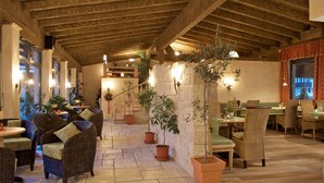 A cozy indoor dining area with wicker furniture, potted plants, and a stone wall. - Allgäuer Kräuteralm (Oberstaufen)