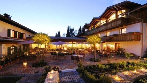 A courtyard with outdoor seating, stone pathways, and a wooden building with balconies. - Allgäuer Kräuteralm (Oberstaufen)