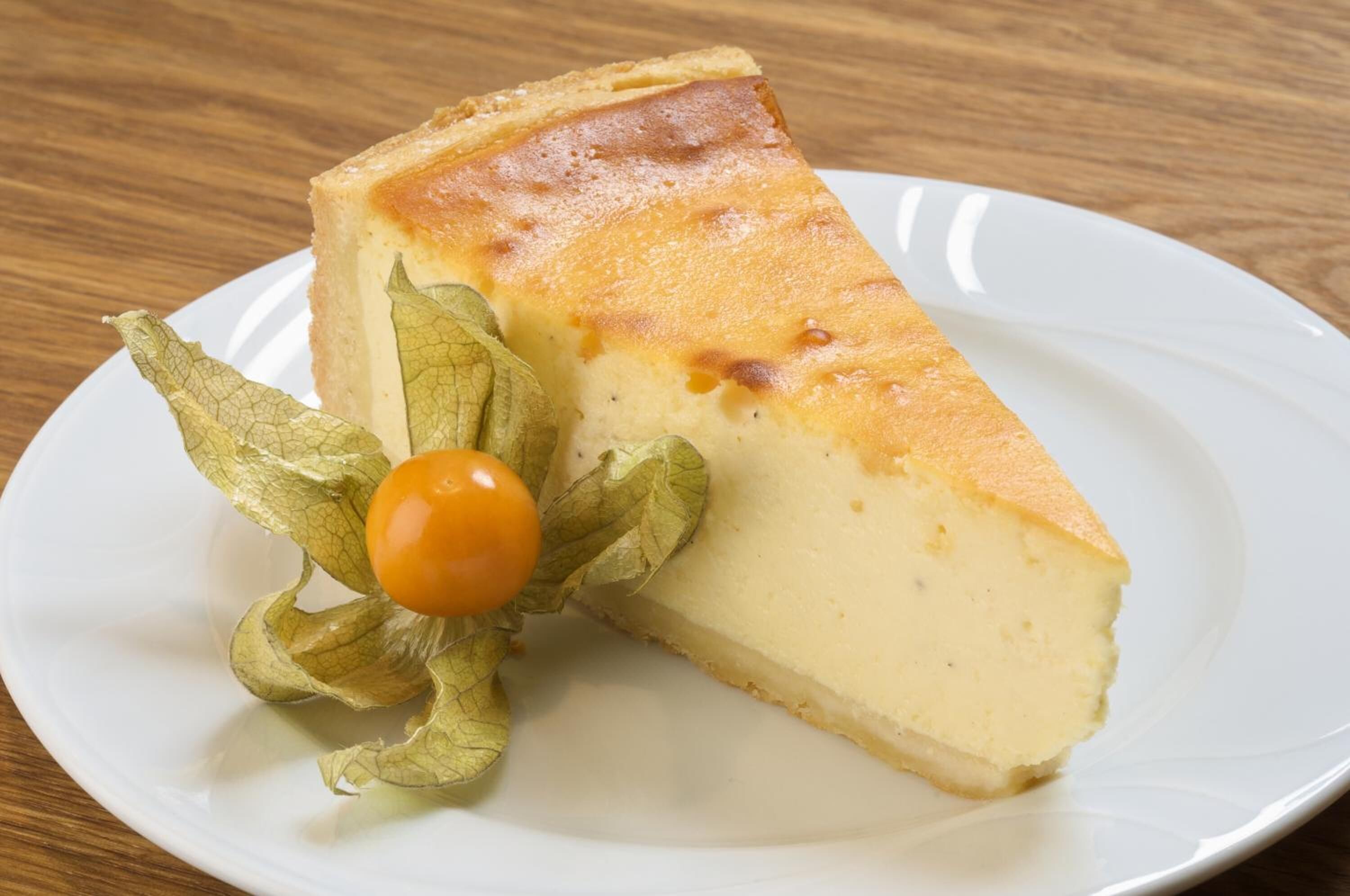 A slice of cheesecake on a white plate with a cherry and a leaf garnish.