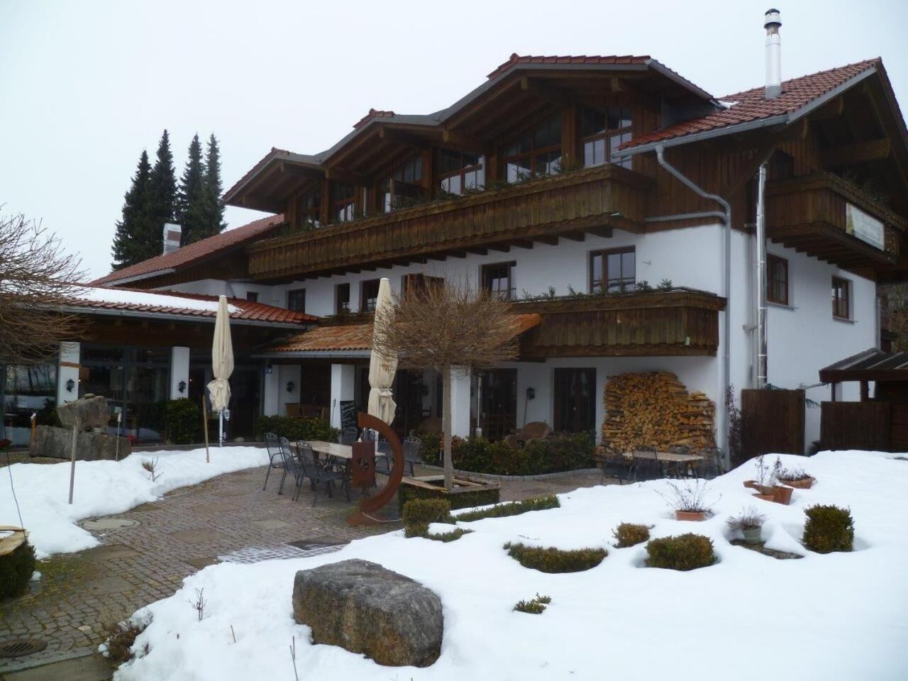Edifici de tipus xalet tradicional amb façana de pedra, balcons de fusta i un pati cobert de neu.