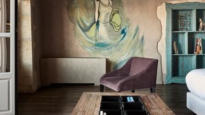 A room with a mural, a purple armchair, a wooden coffee table, and a teal bookshelf.
