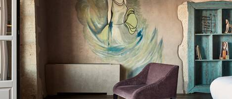 A room with a mural, a purple armchair, a wooden coffee table, and a teal bookshelf.