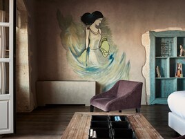 A room with a mural, a purple armchair, a wooden coffee table, and a teal bookshelf.