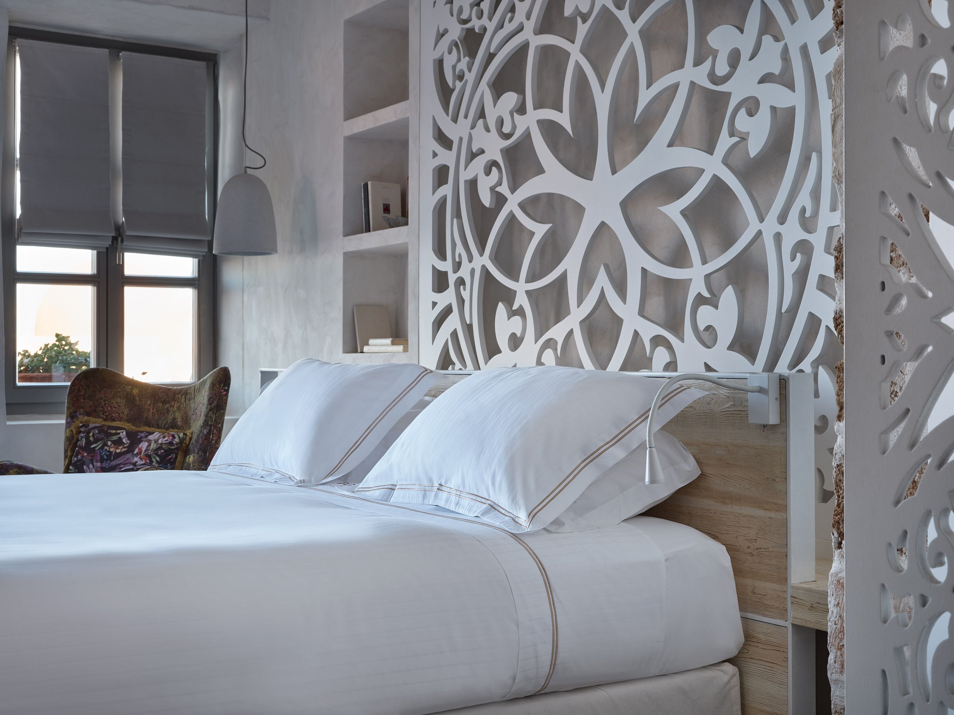 A neatly made bed with white linens and a patterned pillow, a wooden headboard, and a decorative wall panel.