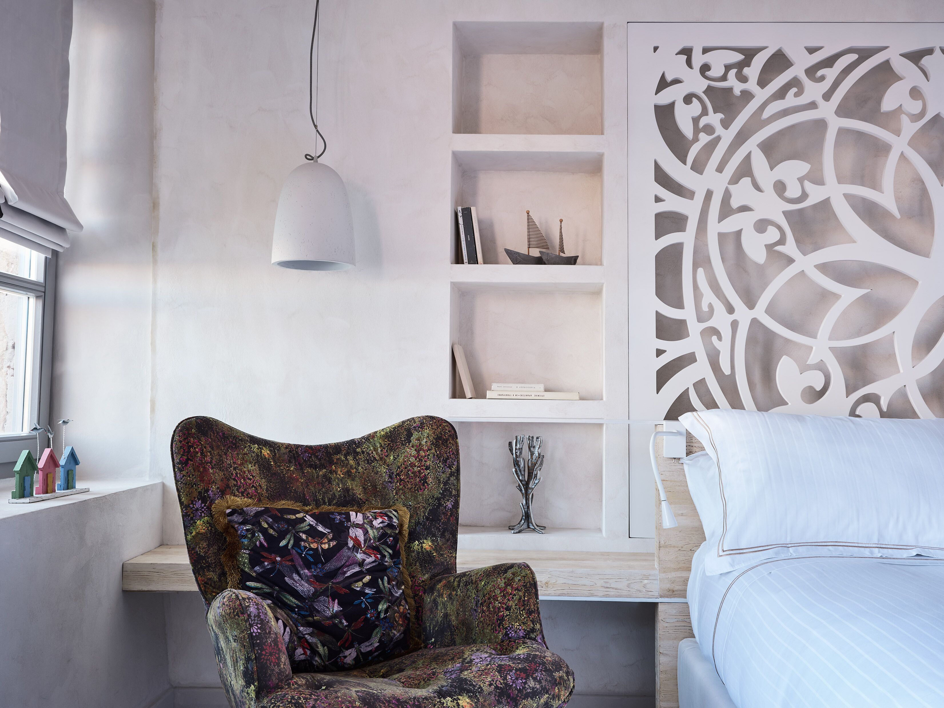 A modern bedroom with a floral armchair, a white bed, and a decorative wall panel.