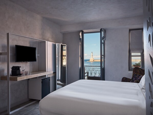 A modern hotel room with a large bed, a TV, a desk with a coffee maker, and a view of a lighthouse through an open door. - Domus Fresco, Member of Domus Elegance Collection (Chania)