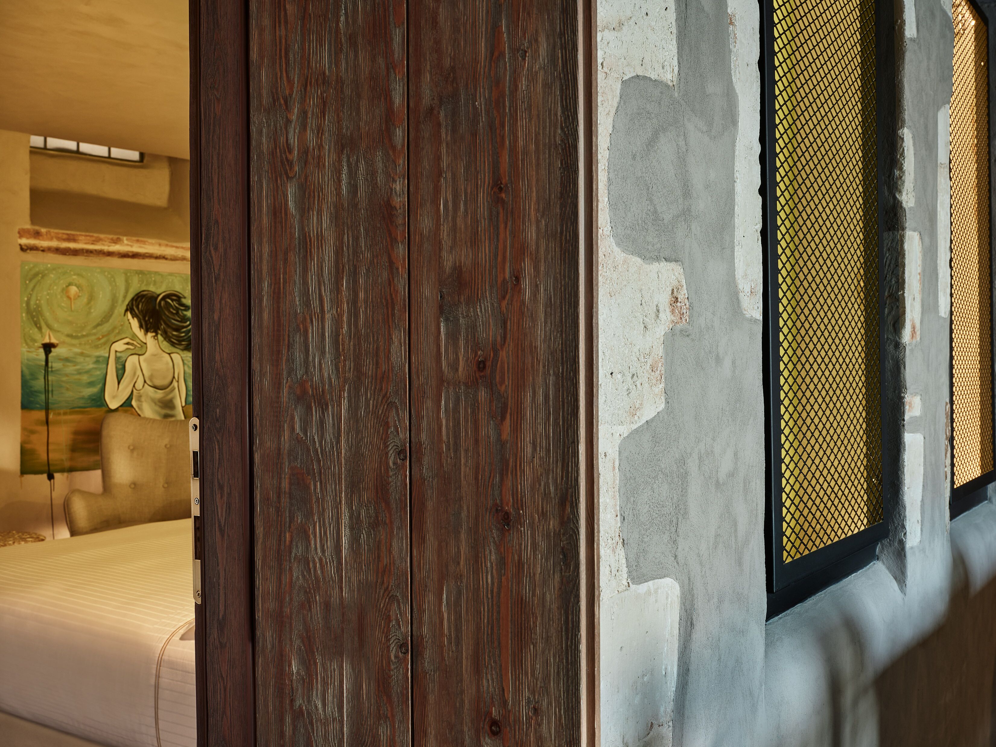 A room with a wooden door, a window with a mesh screen, and a painting on the wall.
