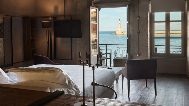 A bedroom with a bed, a chair, a TV, and a view of a lighthouse through a window.