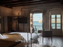 A bedroom with a bed, a chair, a TV, and a view of a lighthouse through a window.